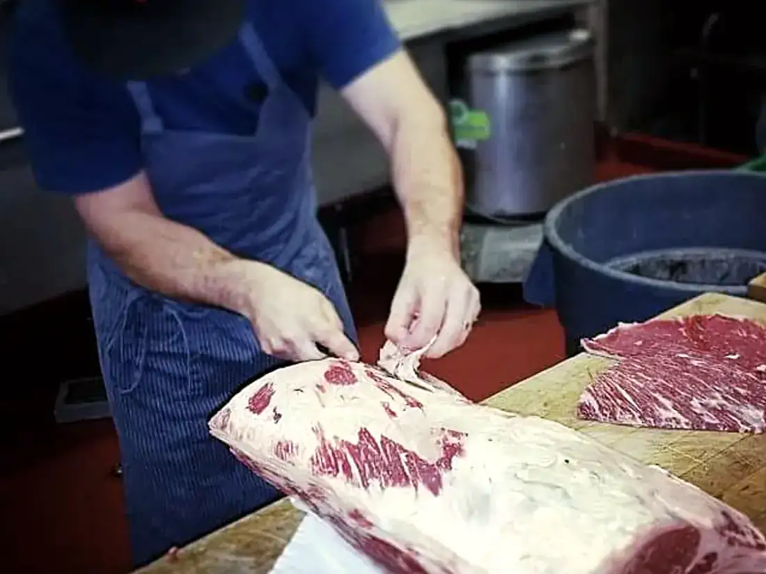 A chef trimming a large wagyu strip loin by hand on a butcher board