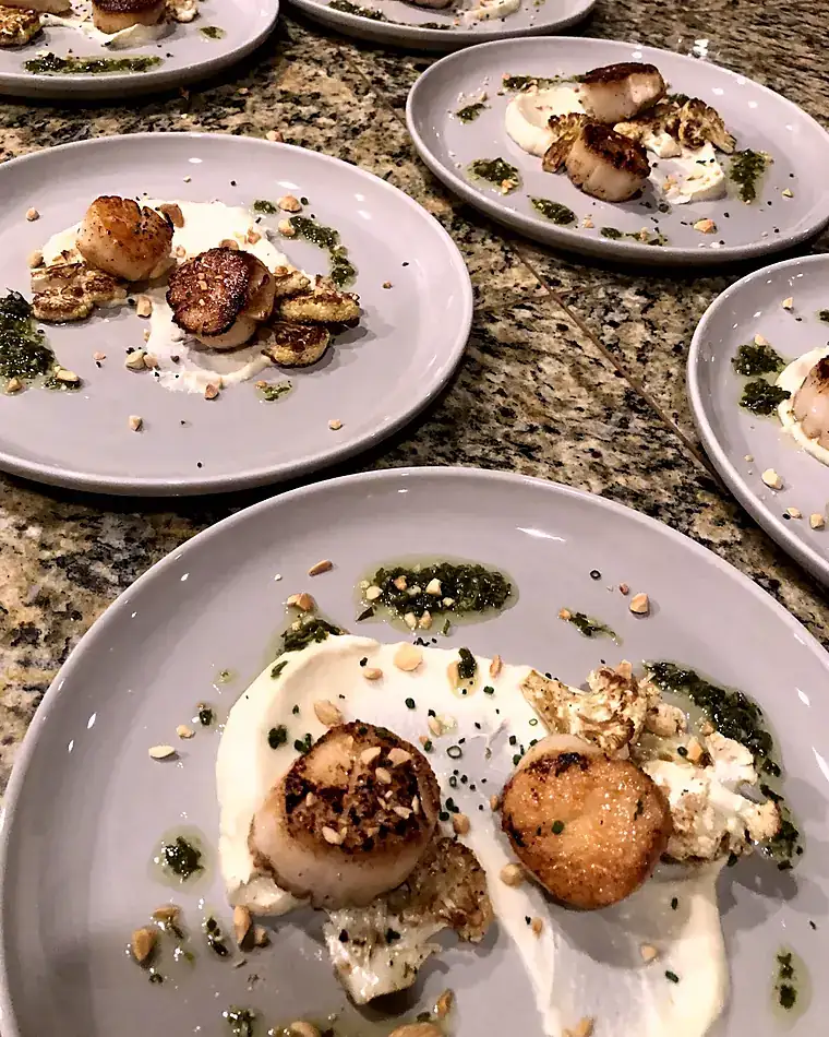 Plates of seared scallops with cauliflower purée, hazelnut and salsa verde lined up for service