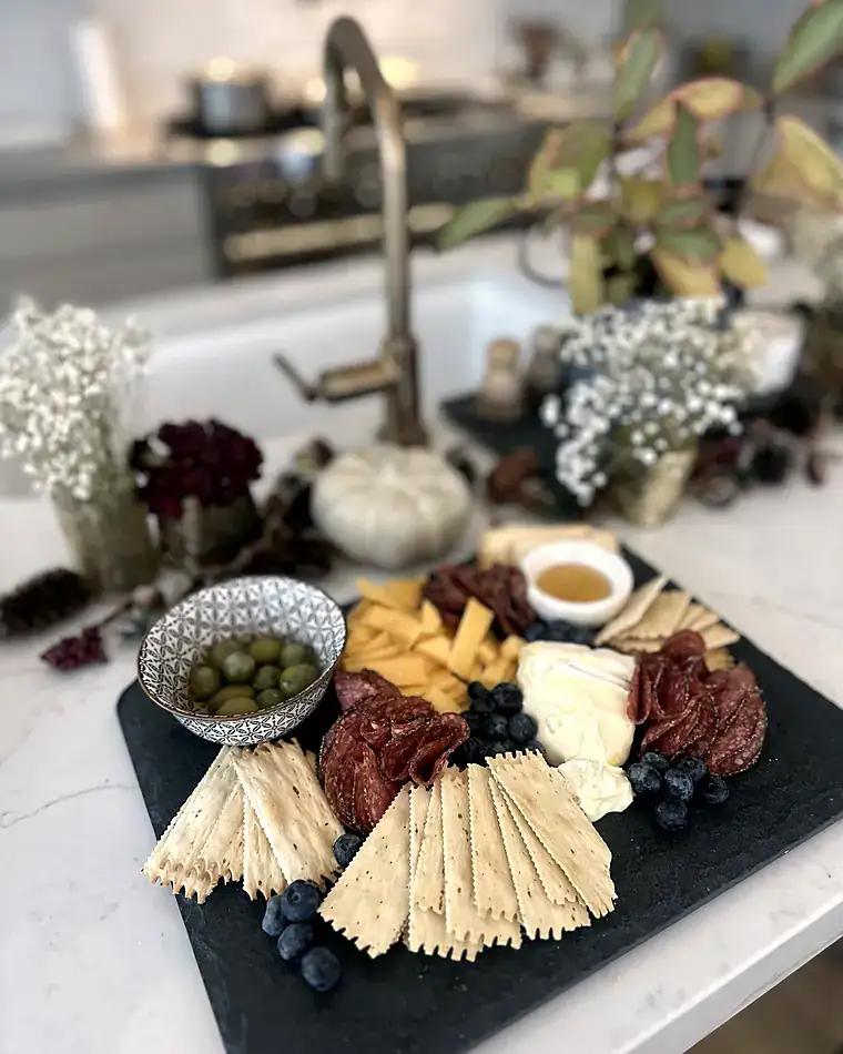 A charcuterie and cheese board styled with florals on a marble counter