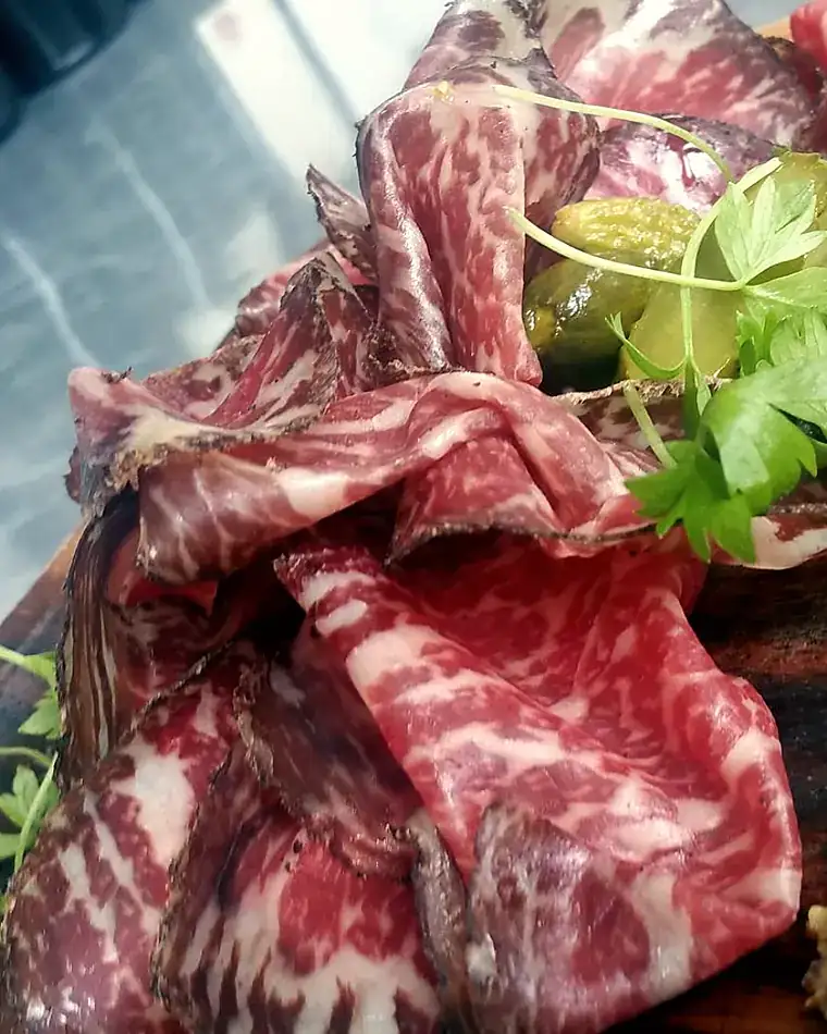 Thinly sliced marbled wagyu draped on a board with celery leaves and cornichon