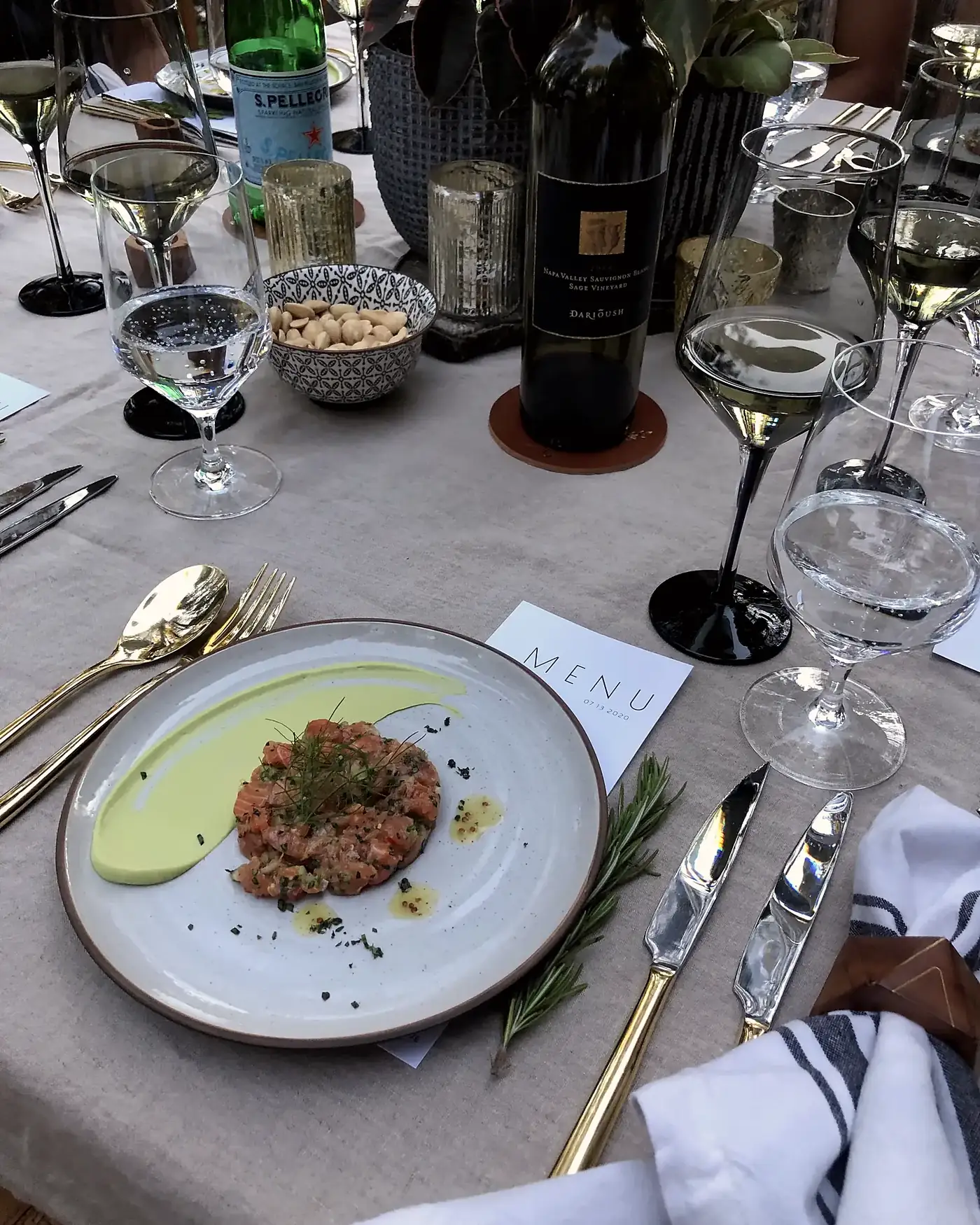 A dressed private dining table with linen, printed menus, crystal, gold flatware and a plated first course