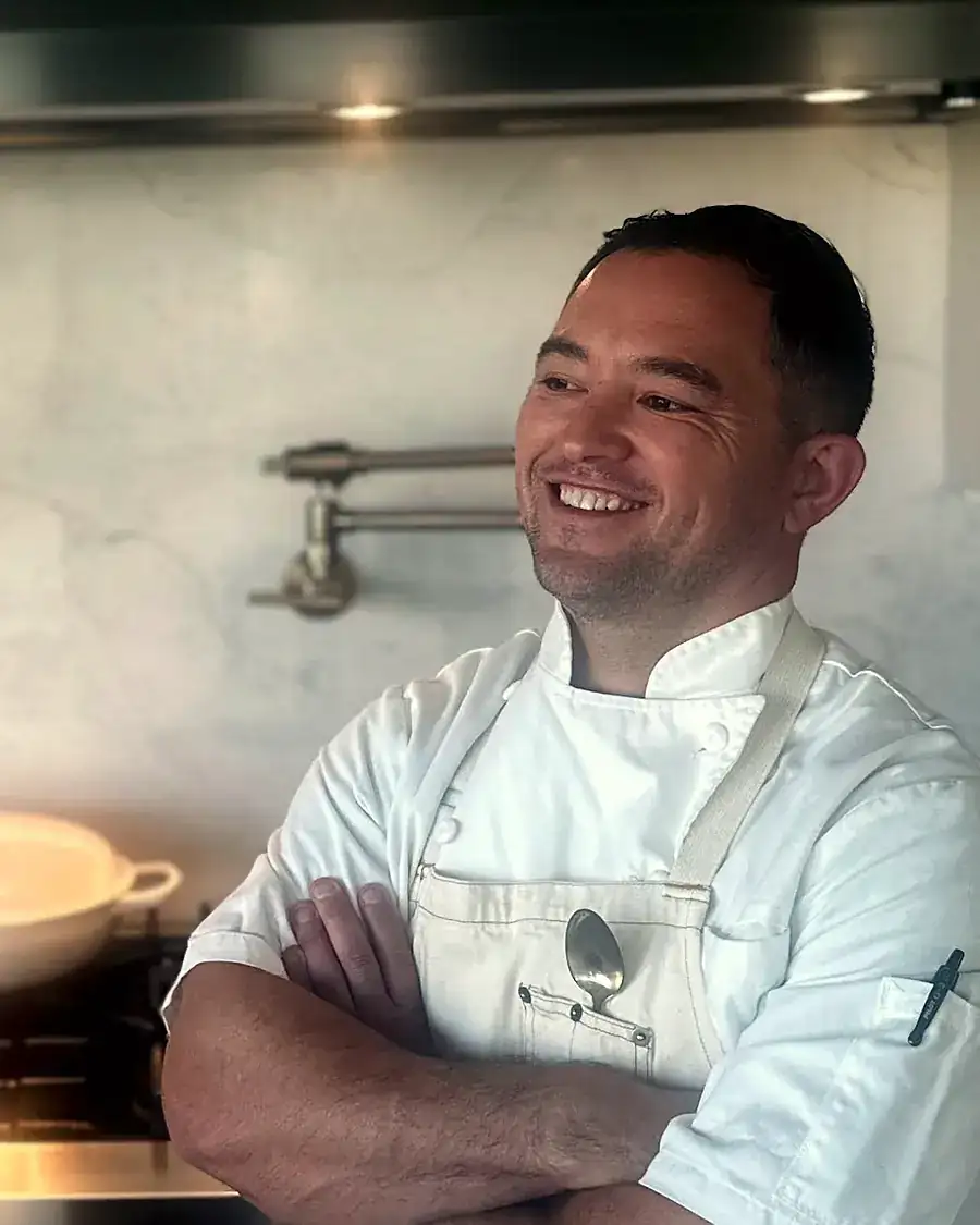 Marc laughing in chef's whites in front of a range